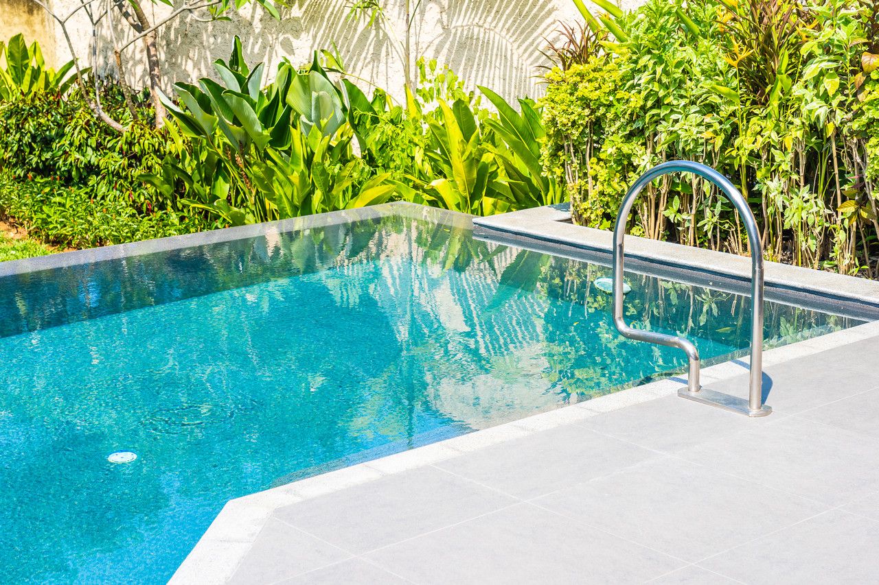 Piscină exterioară cu apă turcoaz, scară din inox și vegetație în jur